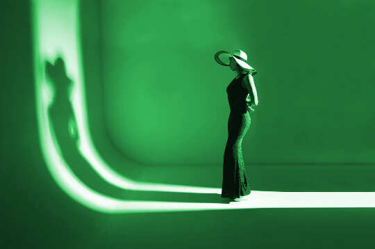 a model standing on a runway facing her shadow... all in green
